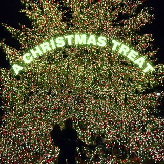 Two sillouttes holding one another against a brightly lit Christmas tree